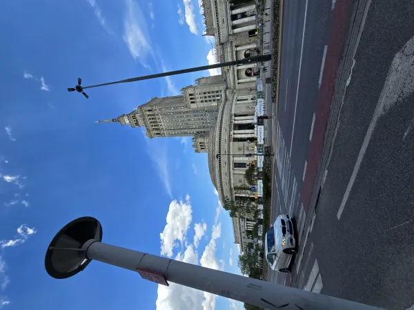A daytime photograph depicts a wide urban street scene with a classic historic building featuring a tall clock tower in